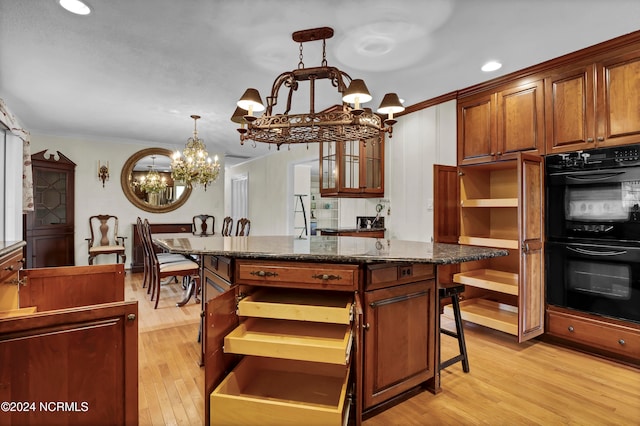 kitchen featuring hanging light fixtures, a kitchen island, a breakfast bar area, black double oven, and light hardwood / wood-style floors