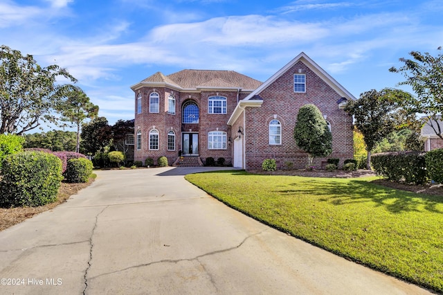 colonial inspired home featuring a garage, brick siding, concrete driveway, and a front yard