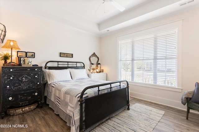 bedroom with a ceiling fan, wood finished floors, visible vents, baseboards, and a tray ceiling