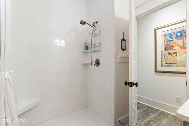 bathroom with a tile shower, baseboards, and wood finished floors