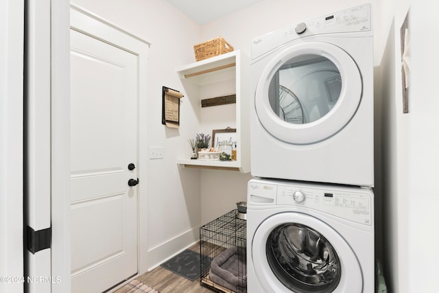 clothes washing area with laundry area, stacked washer and dryer, wood finished floors, and baseboards