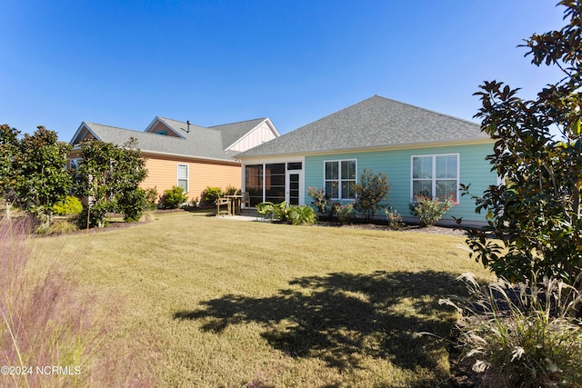 back of house with a yard, a patio, roof with shingles, and a sunroom