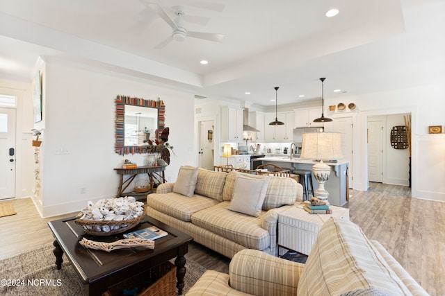 living room with ceiling fan, a raised ceiling, light wood-type flooring, and sink