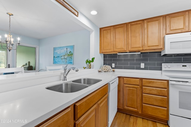 kitchen featuring white appliances, sink, pendant lighting, a chandelier, and light hardwood / wood-style floors