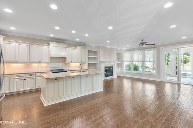 kitchen with custom exhaust hood, a kitchen island with sink, sink, and hardwood / wood-style flooring