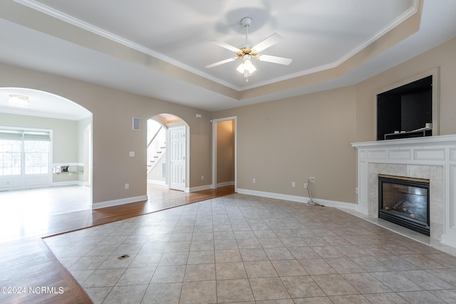 unfurnished living room with crown molding, arched walkways, a tile fireplace, a ceiling fan, and stairs