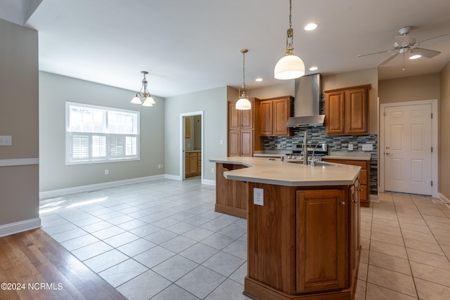 kitchen featuring wall chimney exhaust hood, tasteful backsplash, a center island with sink, and pendant lighting