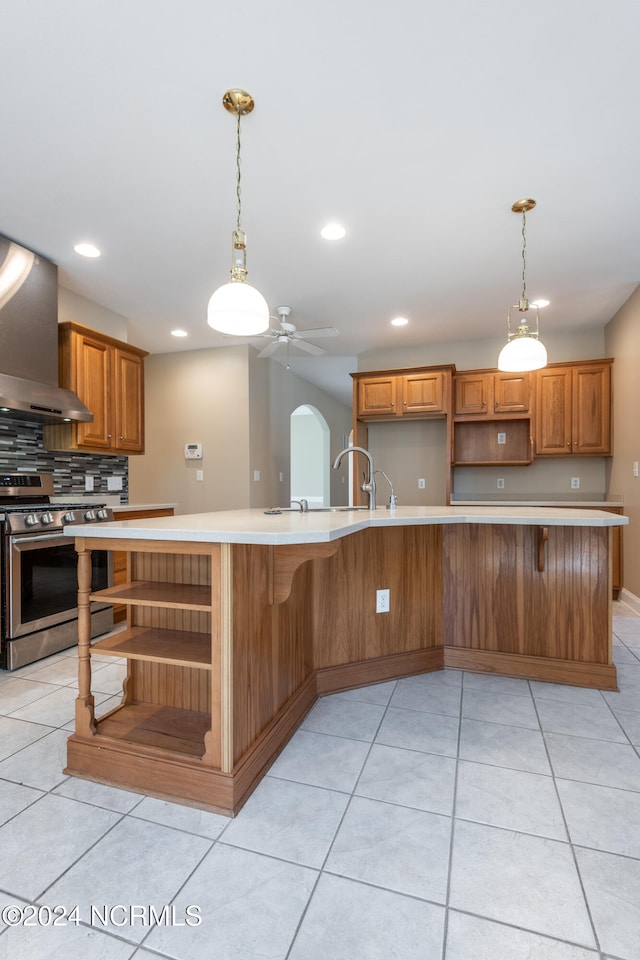 kitchen with ceiling fan, wall chimney range hood, light tile patterned flooring, and stainless steel stove