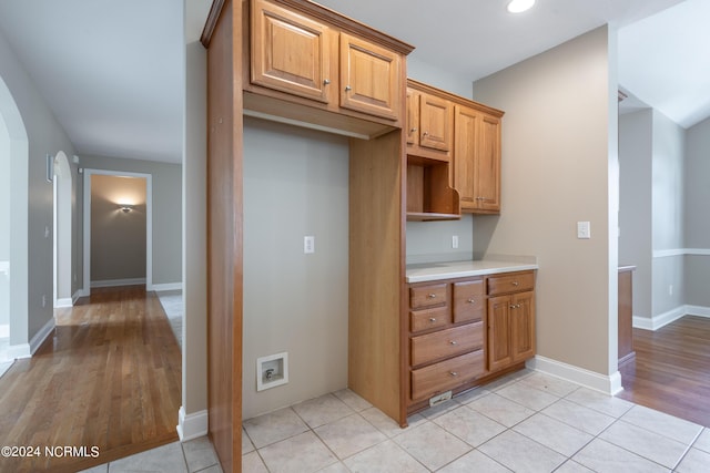 kitchen with arched walkways, light wood-style floors, brown cabinetry, and light countertops