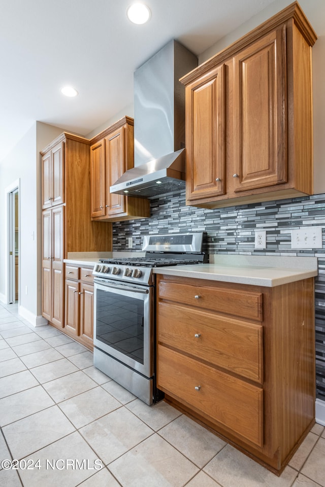 kitchen with wall chimney exhaust hood, tasteful backsplash, stainless steel stove, and light tile patterned floors