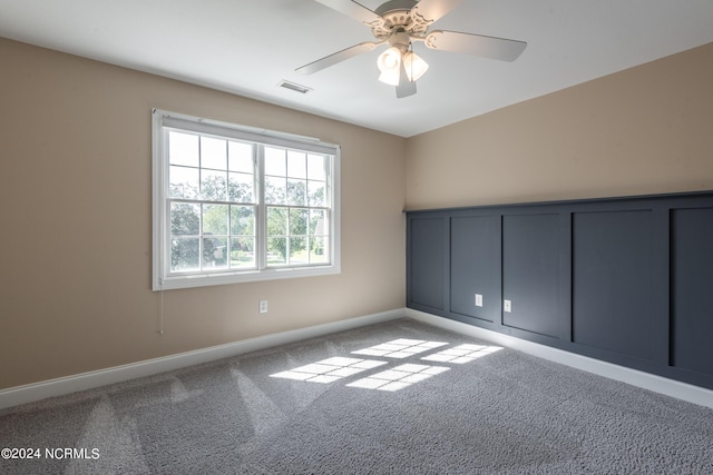 unfurnished room featuring carpet floors, a decorative wall, ceiling fan, baseboards, and visible vents