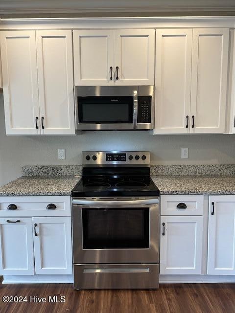 kitchen featuring white cabinets, dark hardwood / wood-style floors, light stone counters, and appliances with stainless steel finishes