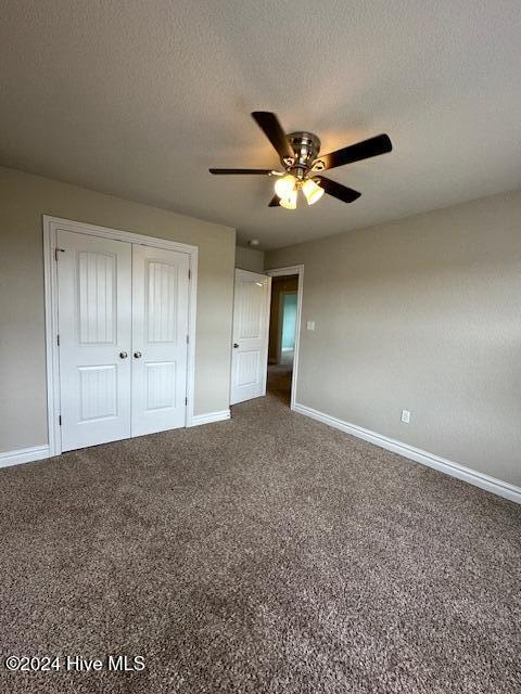 unfurnished bedroom with carpet flooring, ceiling fan, a textured ceiling, and a closet