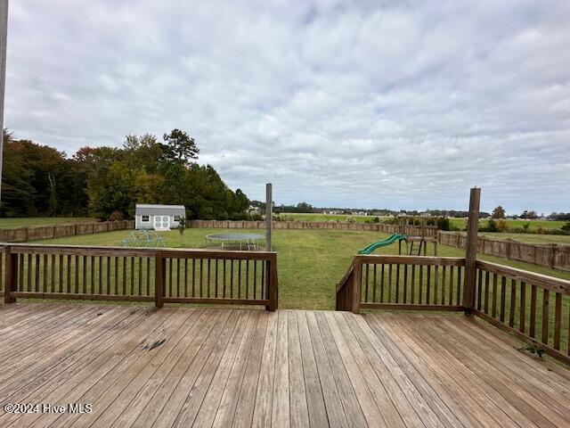 wooden deck with a lawn, a playground, an outdoor structure, and a trampoline