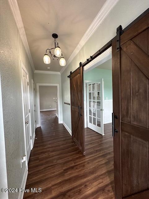 hall with dark hardwood / wood-style flooring, a barn door, an inviting chandelier, and ornamental molding