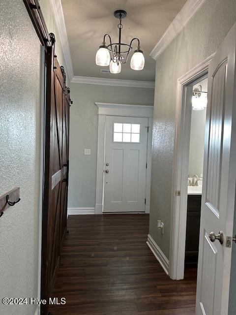 interior space with a barn door, crown molding, dark hardwood / wood-style flooring, and a chandelier