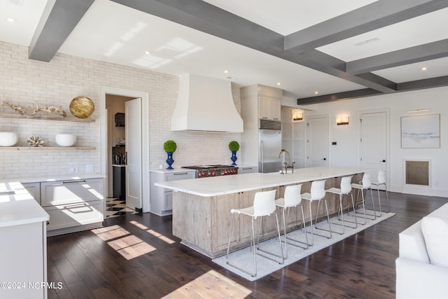 kitchen with dark hardwood / wood-style floors, a breakfast bar area, a center island with sink, custom exhaust hood, and appliances with stainless steel finishes