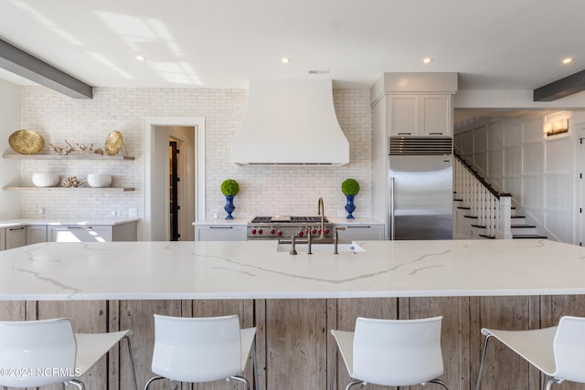 kitchen with backsplash, appliances with stainless steel finishes, a kitchen island, custom range hood, and light stone counters