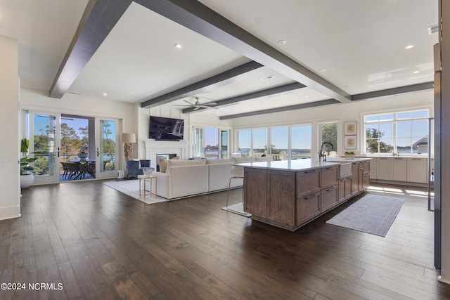 kitchen featuring dark wood-type flooring, beamed ceiling, and a kitchen island with sink