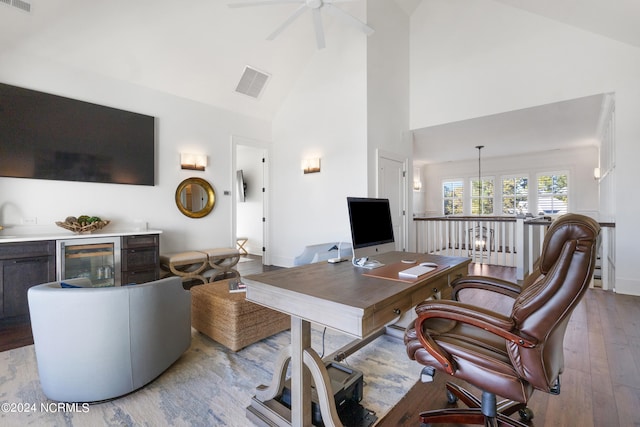 office with light hardwood / wood-style flooring, ceiling fan with notable chandelier, high vaulted ceiling, and beverage cooler