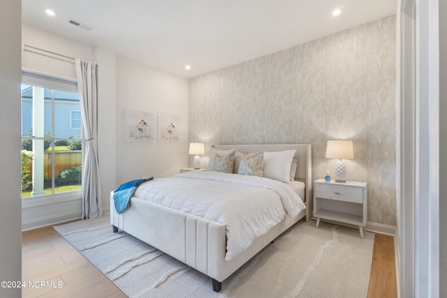 bedroom with multiple windows, a water view, and light wood-type flooring