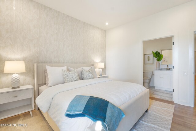 bedroom with light hardwood / wood-style flooring, ensuite bathroom, and sink