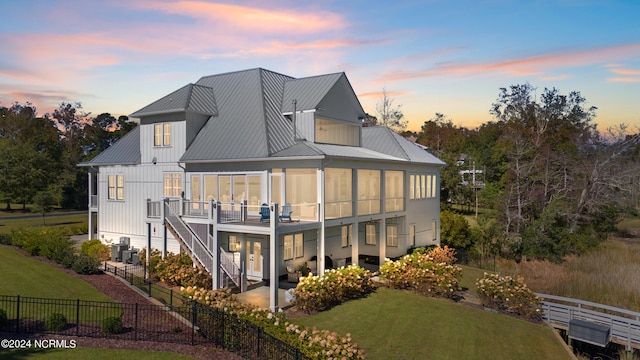 back house at dusk with a patio, a lawn, and a balcony