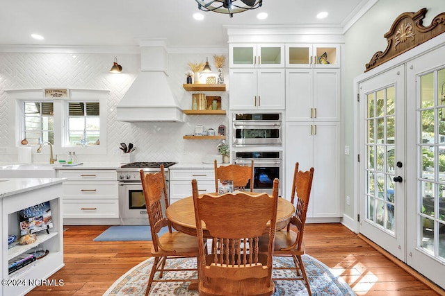 dining area featuring sink, light wood-type flooring, french doors, crown molding, and a chandelier