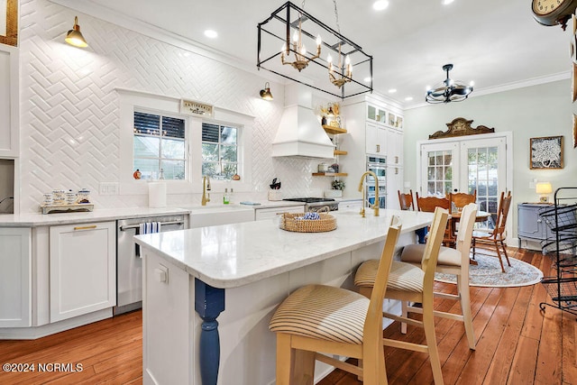 kitchen featuring ornamental molding, an island with sink, light hardwood / wood-style flooring, and white cabinets