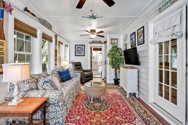 living room with wood walls, crown molding, and ceiling fan