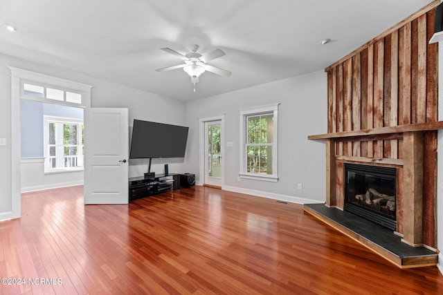 unfurnished living room with hardwood / wood-style flooring, a large fireplace, ceiling fan, and a wealth of natural light