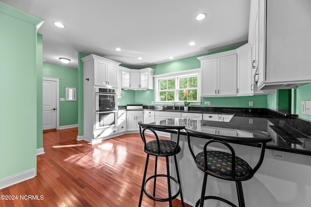 kitchen with white cabinetry, a kitchen bar, wood-type flooring, and kitchen peninsula