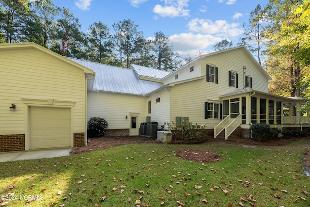 rear view of property with a yard, a sunroom, central air condition unit, and a garage