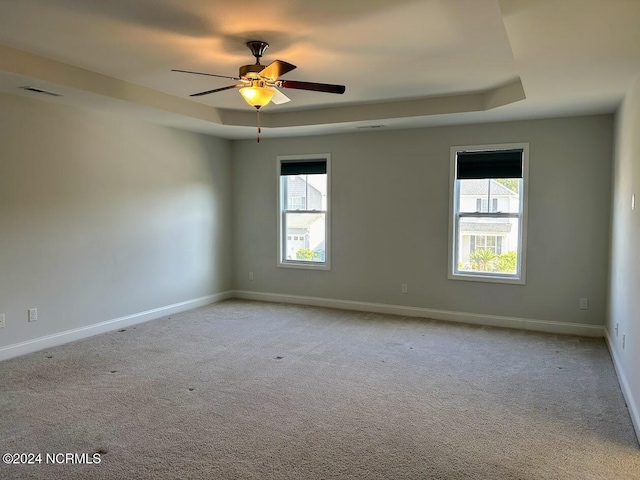 empty room with light carpet, a raised ceiling, a wealth of natural light, and ceiling fan