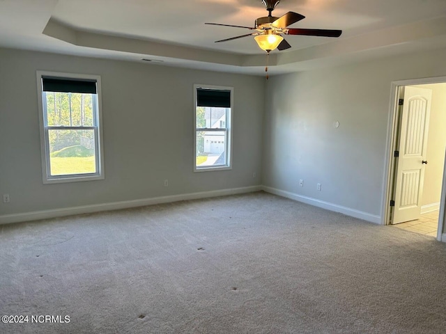 carpeted spare room with ceiling fan and a tray ceiling