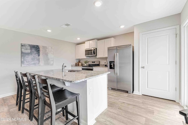 kitchen with appliances with stainless steel finishes, white cabinetry, a center island with sink, light stone countertops, and a kitchen bar