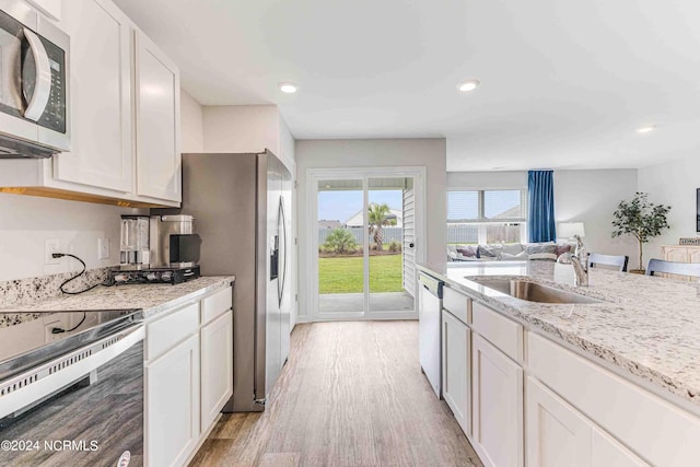 kitchen featuring sink, white cabinetry, stainless steel appliances, light stone counters, and light hardwood / wood-style floors