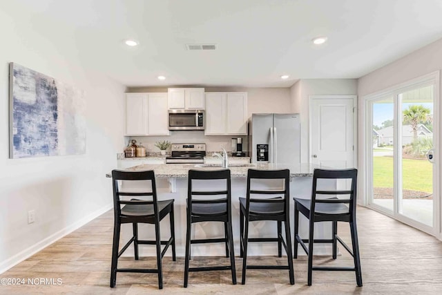 kitchen featuring appliances with stainless steel finishes, a kitchen breakfast bar, light stone counters, an island with sink, and white cabinets