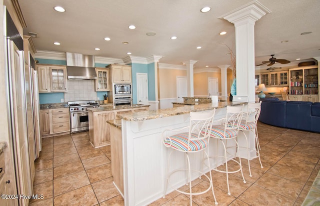 kitchen featuring ceiling fan, stainless steel appliances, wall chimney range hood, and a breakfast bar