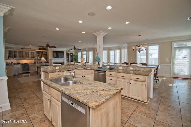 kitchen featuring sink, decorative columns, stainless steel dishwasher, crown molding, and a kitchen island with sink