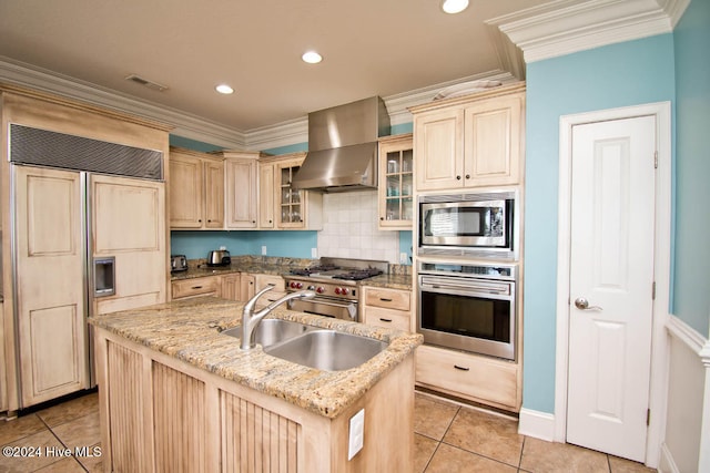 kitchen featuring sink, wall chimney exhaust hood, built in appliances, light brown cabinets, and a kitchen island with sink