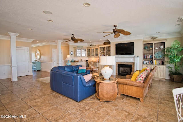 tiled living room featuring a tiled fireplace, ceiling fan, a textured ceiling, ornate columns, and crown molding