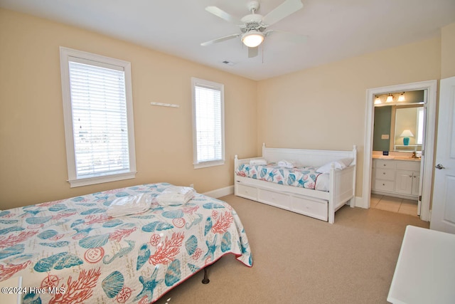 carpeted bedroom featuring ensuite bath, multiple windows, and ceiling fan