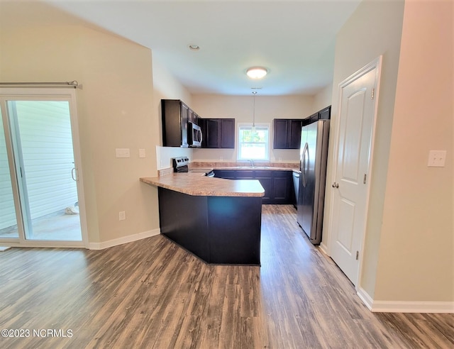 kitchen with appliances with stainless steel finishes, kitchen peninsula, hardwood / wood-style floors, and pendant lighting