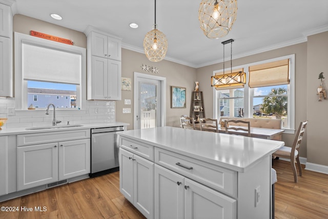 kitchen featuring light countertops, stainless steel dishwasher, a sink, and pendant lighting