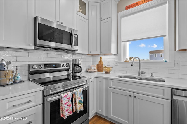 kitchen featuring stainless steel appliances, a sink, white cabinetry, light countertops, and backsplash