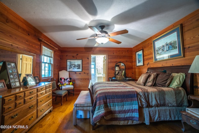 bedroom featuring wood walls, ensuite bath, a textured ceiling, hardwood / wood-style floors, and ceiling fan