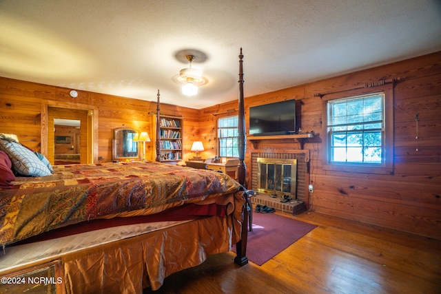 bedroom featuring wooden walls, wood-type flooring, and a brick fireplace