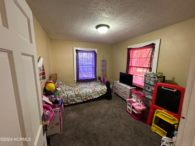 bedroom with a textured ceiling, multiple windows, and dark colored carpet