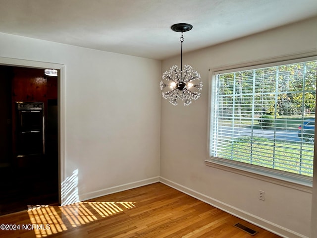 unfurnished dining area with a notable chandelier and hardwood / wood-style flooring